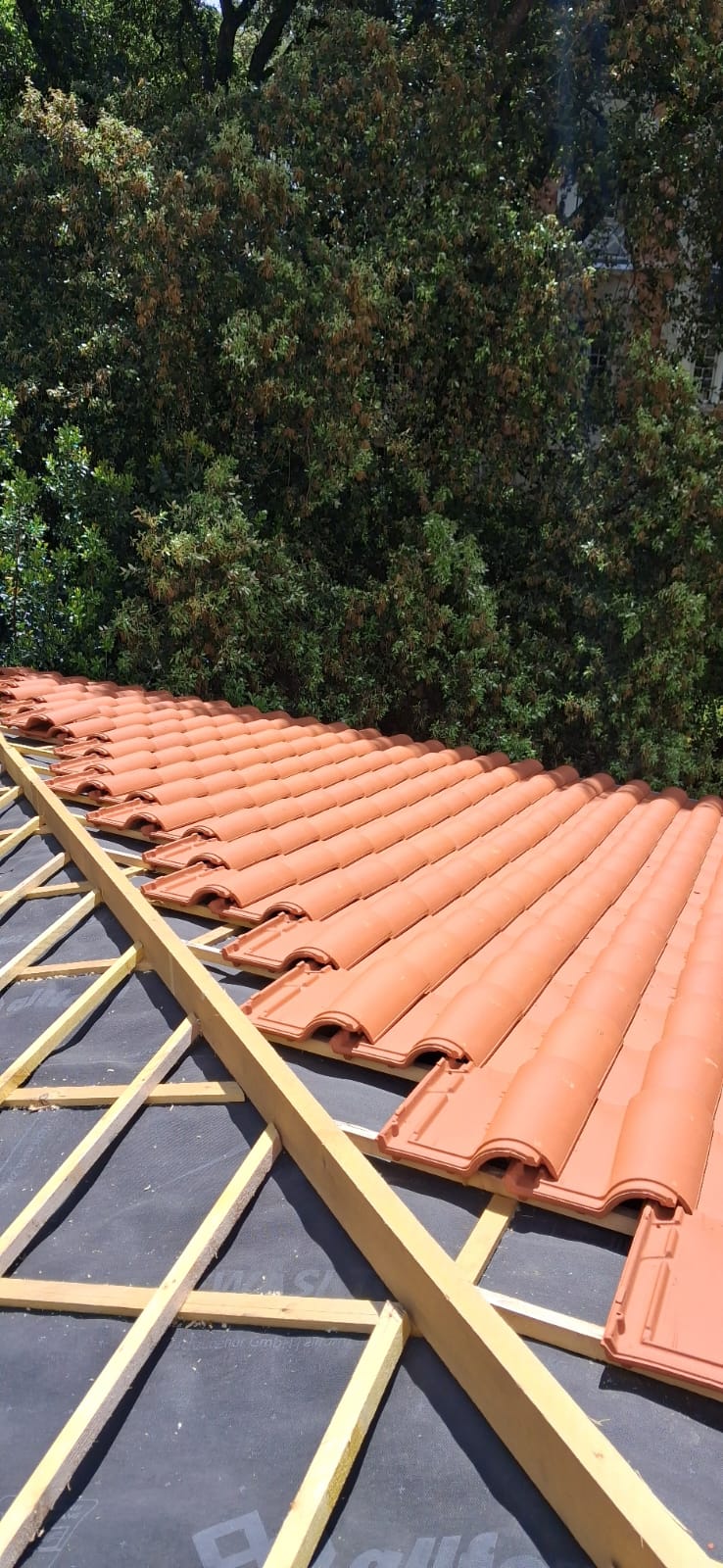 Toiture en cours de pose : lattis et sous-toiture visibles à gauche, tuiles romanes posées à droite — Royan, Charente-Maritime